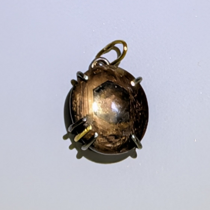 A small oval pendant with a smoky brown translucent center and a gold-tone bail, photographed on a plain light background.