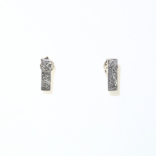A pair of silver-toned rectangular huggie hoop earrings with a textured, hammered metallic finish, displayed on a clean white background.