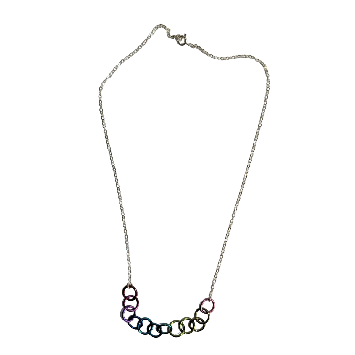 A silver chain necklace featuring a curved bar of interlocking rings in an iridescent rainbow finish, displayed against a solid white background.