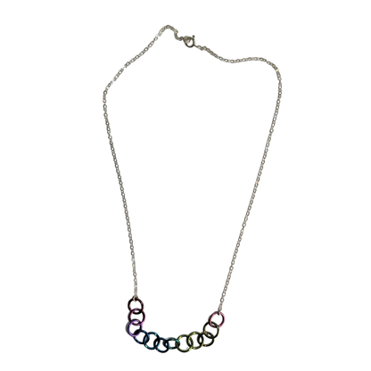 A silver chain necklace featuring a curved bar of interlocking rings in an iridescent rainbow finish, displayed against a solid white background.