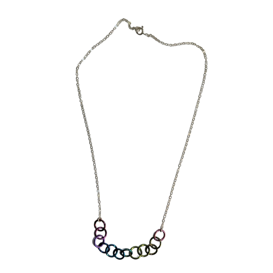 A silver chain necklace featuring a curved bar of interlocking rings in an iridescent rainbow finish, displayed against a solid white background.